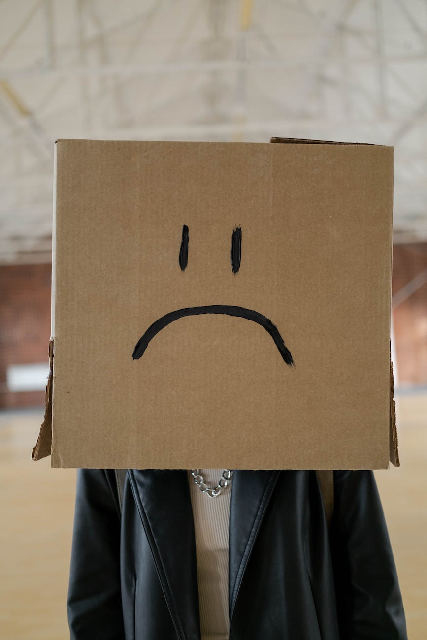 woman with a box on her head with a sad face drawn on it
